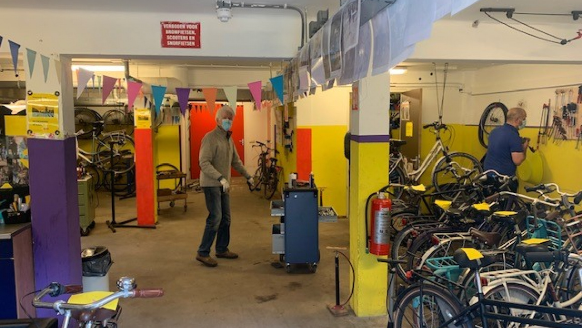 fietsenwerkplaats met gekleurde pilaren, veel fietsen en klussende mense