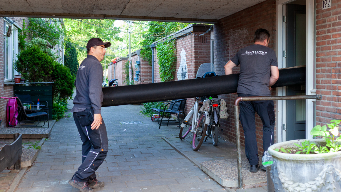 Twee mannen van ed Buurtservice brengen rol tapijt binnen in een woning