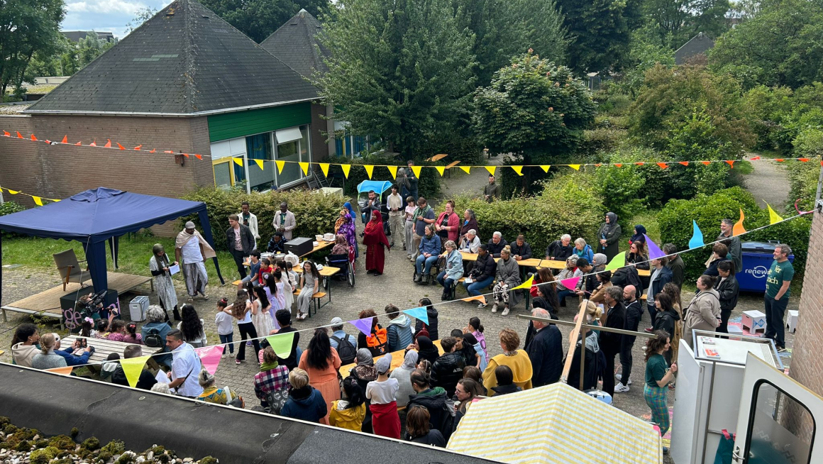 Een grote groep mensen komt samen op het Vergezichtenfestival in Arnhem. Er hangen vlaggetjes en er zijn sprekers.