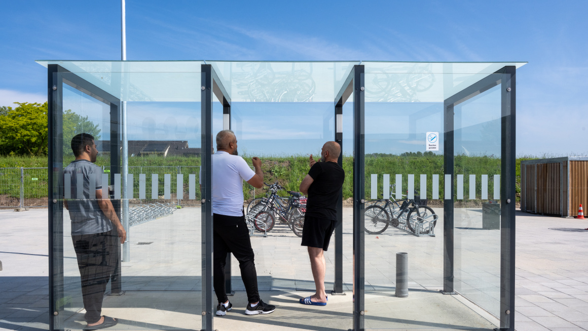 3 mannelijke asielzoekers staan in een glazen rookruimte buiten.