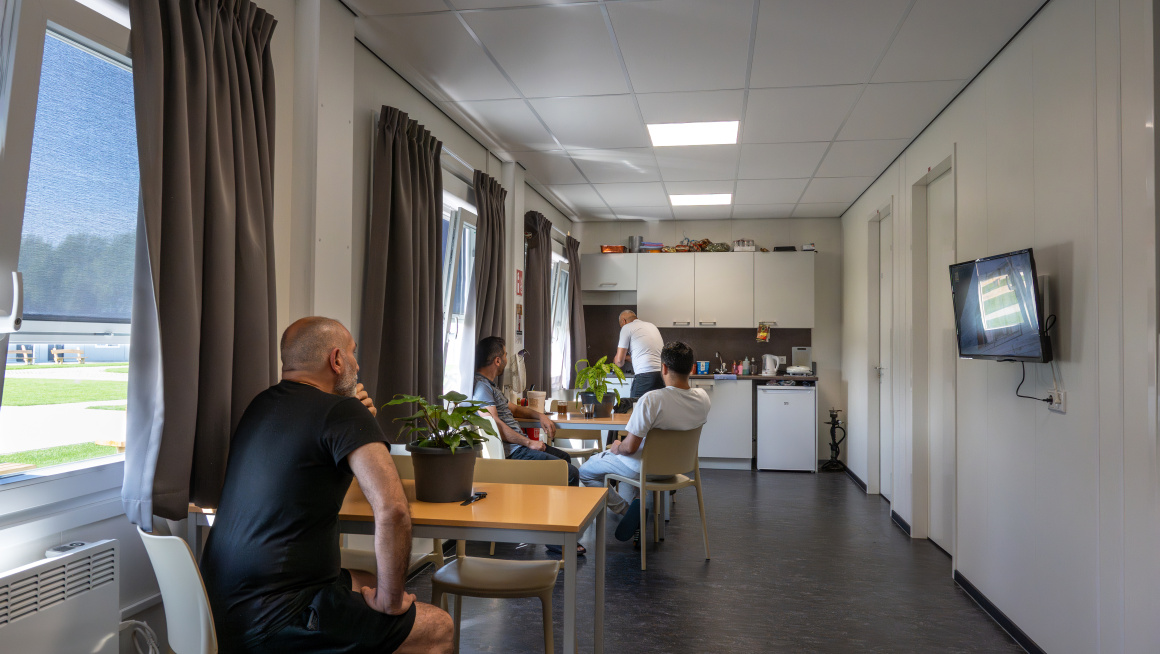 4 mannen zitten in de gemeenschappelijke ruimte van hun woonunit waar de keuken is.