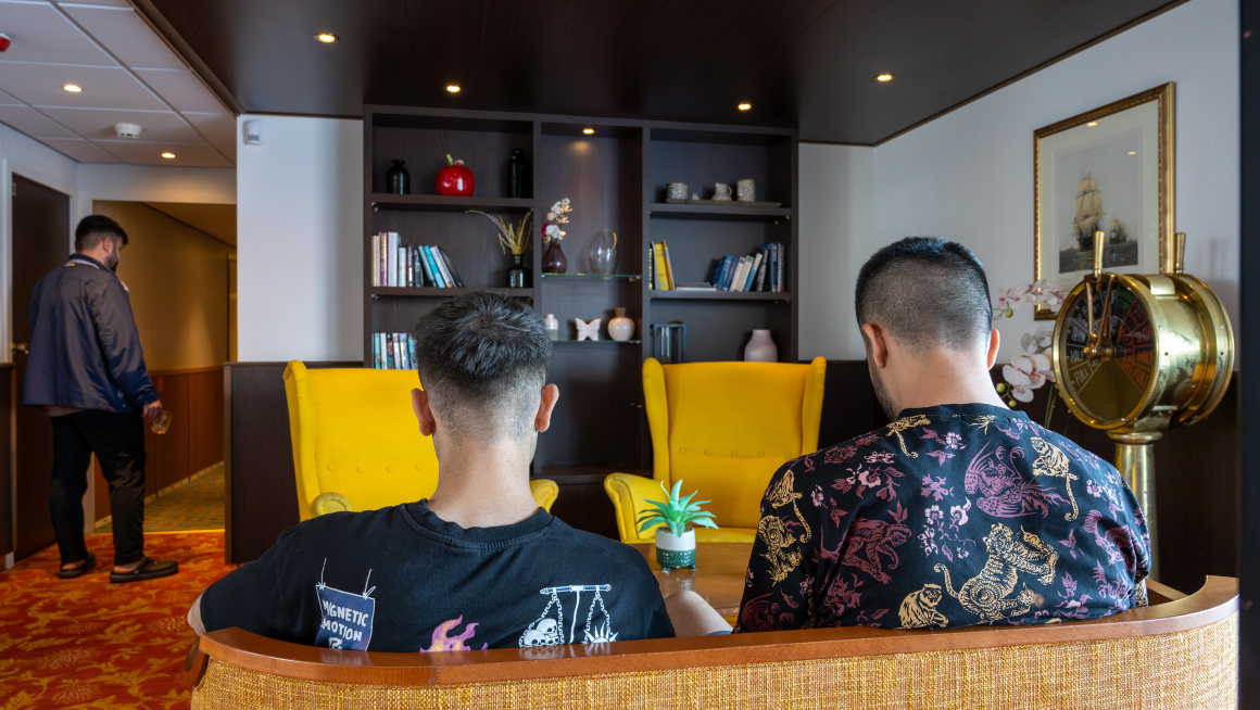 Twee mannen zitten op de bank in de woonkamer van een asielboot.