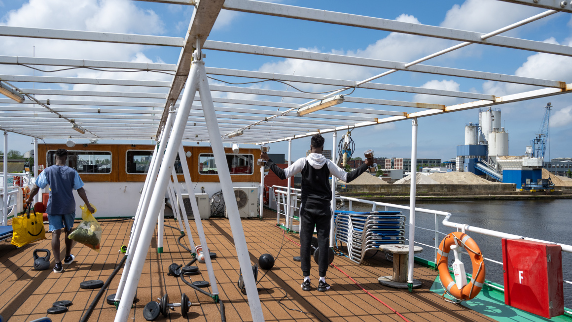 Twee mannen zijn aan het fitnessen op het dek van een asielboot.