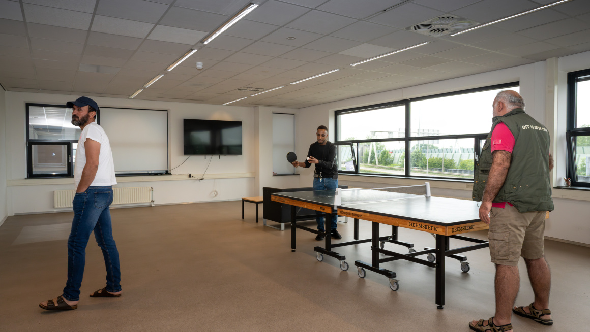 Medewerker en asielzoeker spelen tafeltennis in de recreatieruimte.
