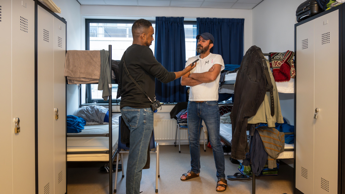 Medewerker en statushouder zijn in gesprek in zijn slaapkamer waar 2 stapelbedden en 4 kasten staan.
