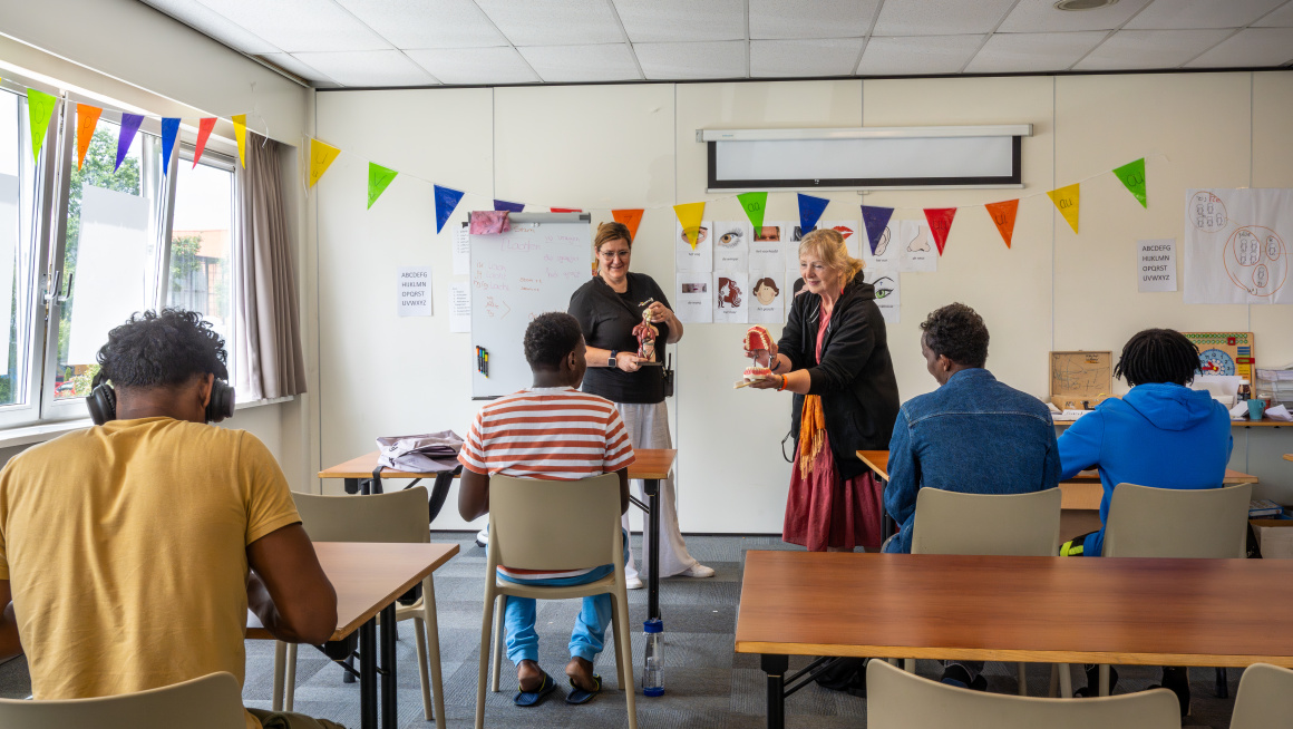 4 asielzoekers leren in een klaslokaal van twee vrijwilligsters over gezondheid