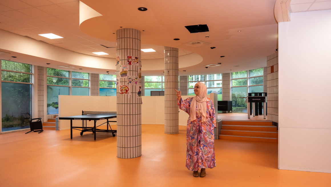 Medewerkster staat in de lege recreatieruimte waar een tafeltennistafel staat.