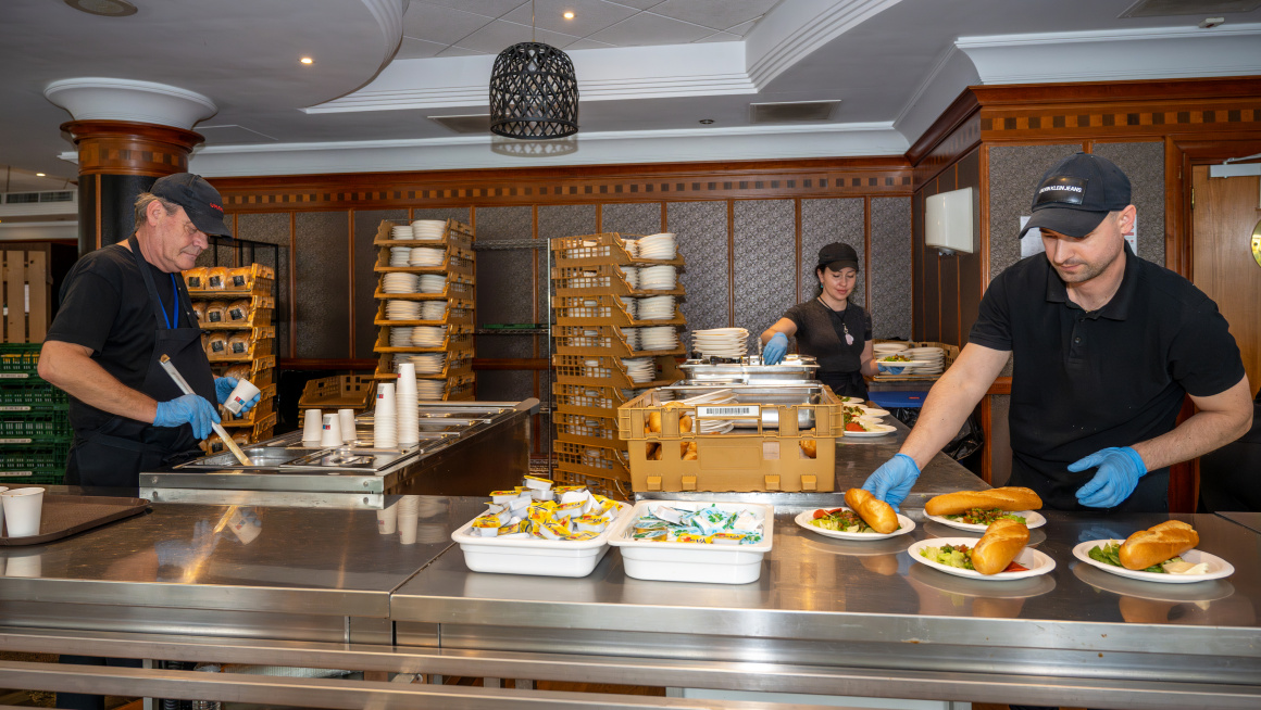 Drie personeelsleden van het hotel maken in de keuken de maaltijd voor de asielzoekers klaar. 
