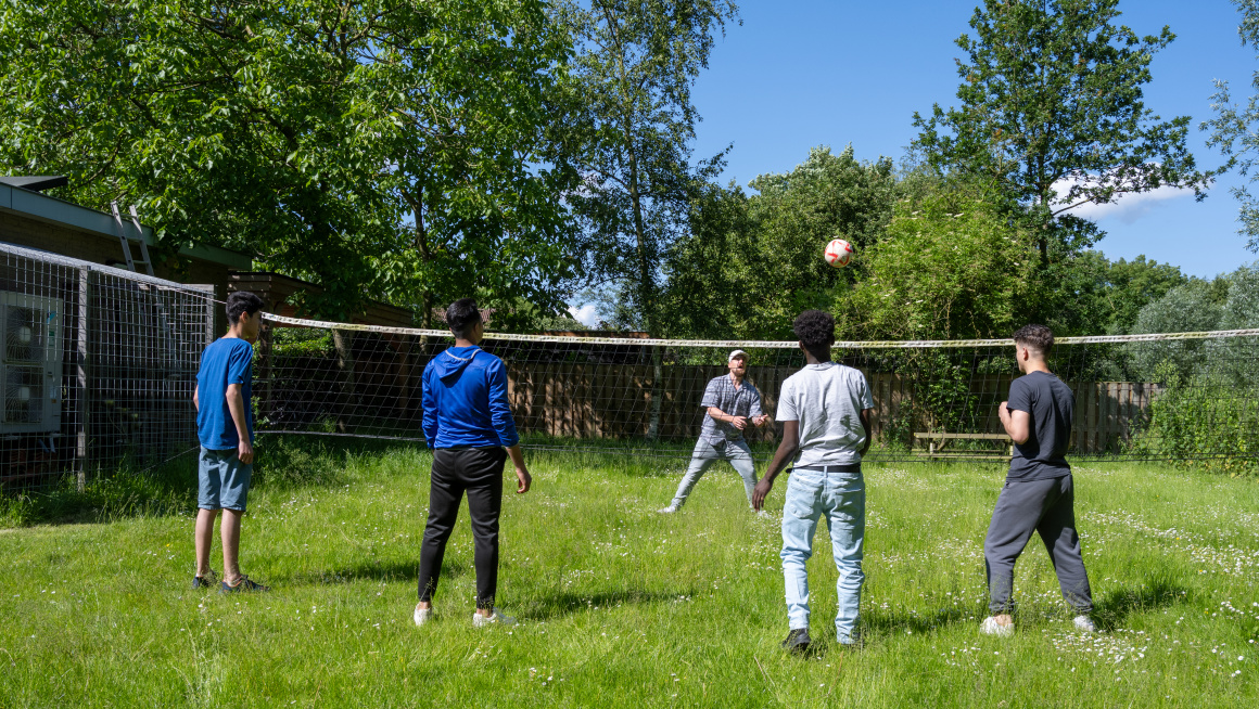 4 minderjarige jongens spelen volleybal in de tuin met een medewerker