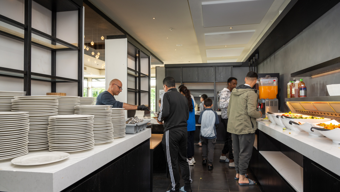 Volwassenen en kinderen scheppen eten op bij het buffet.