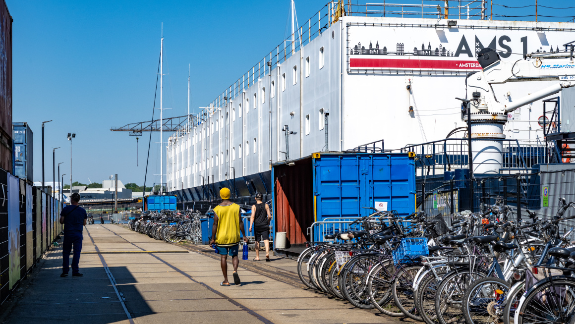Veel fietsen op de kade naast het drijvend ponton met daarop woonunits.