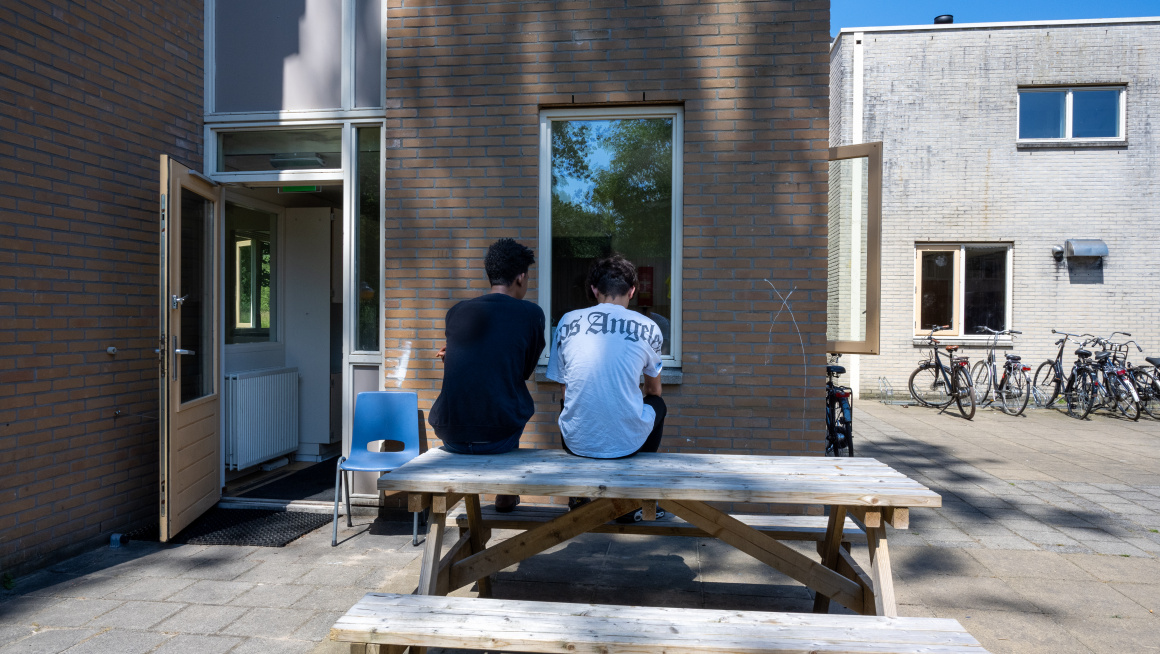 2 minderjarige jongens zitten buiten op de picknicktafel bij hun opvanglocatie.