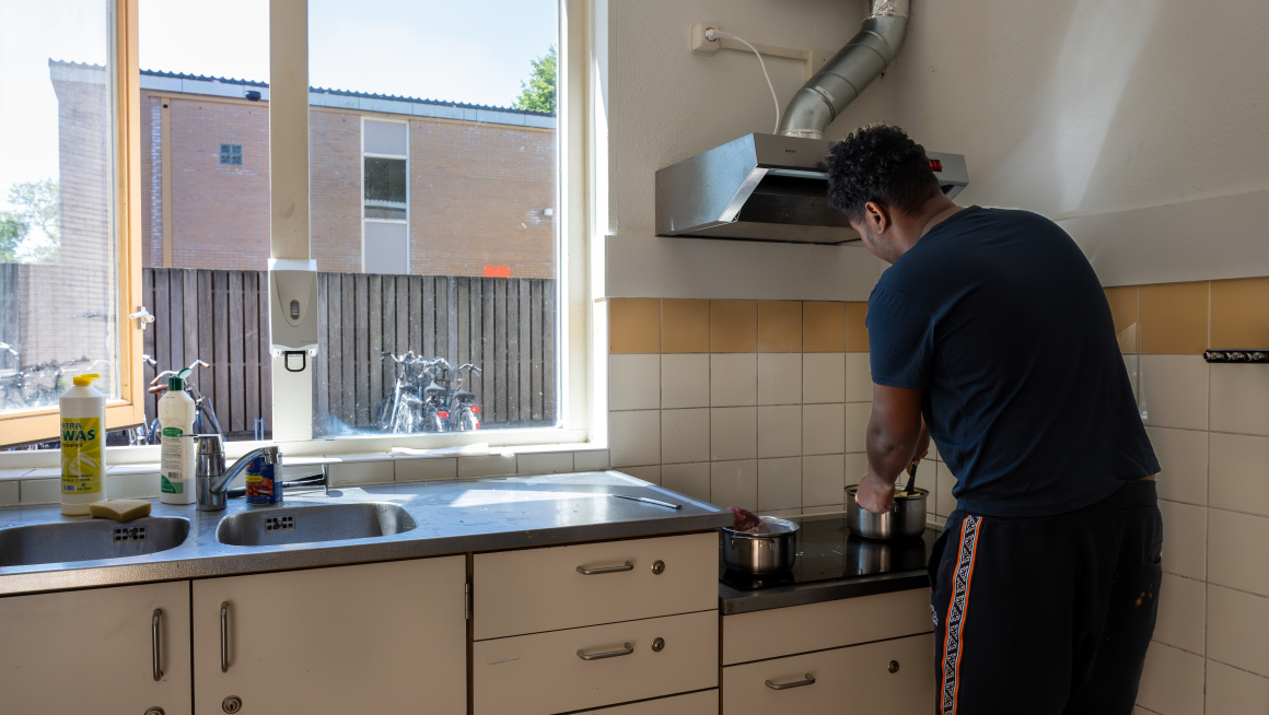 Minderjarige jongen kookt eten op het fornuis in de keuken.