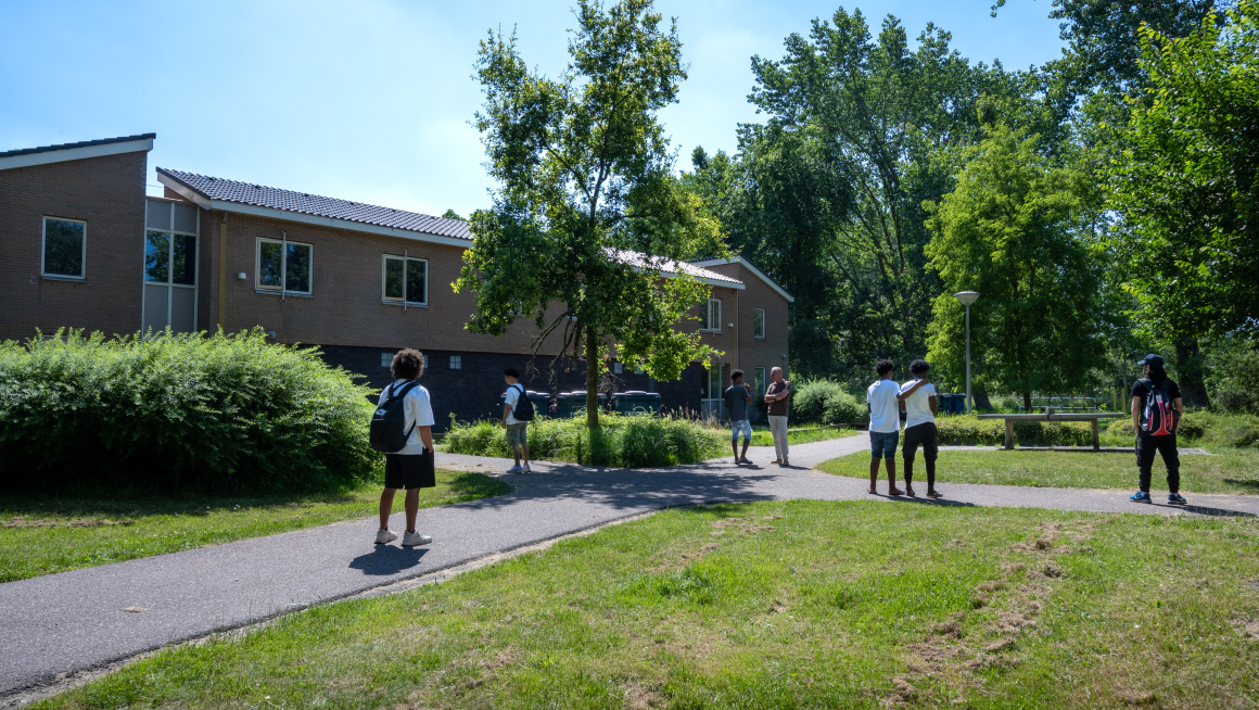 Diverse minderjarige jongens lopen over de paden in het groen rondom hun opvanglocatie.