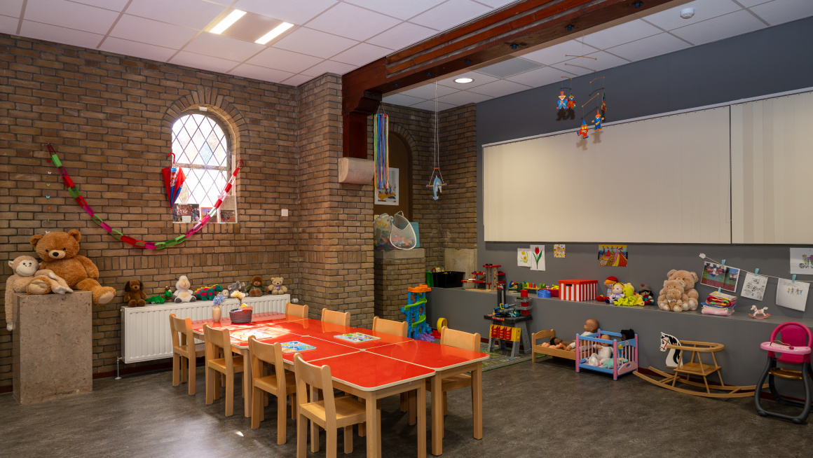 Kinderopvanglokaal met tafels en stoelen en speelgoed in azc Apeldoorn, er zijn geen kinderen aanwezig