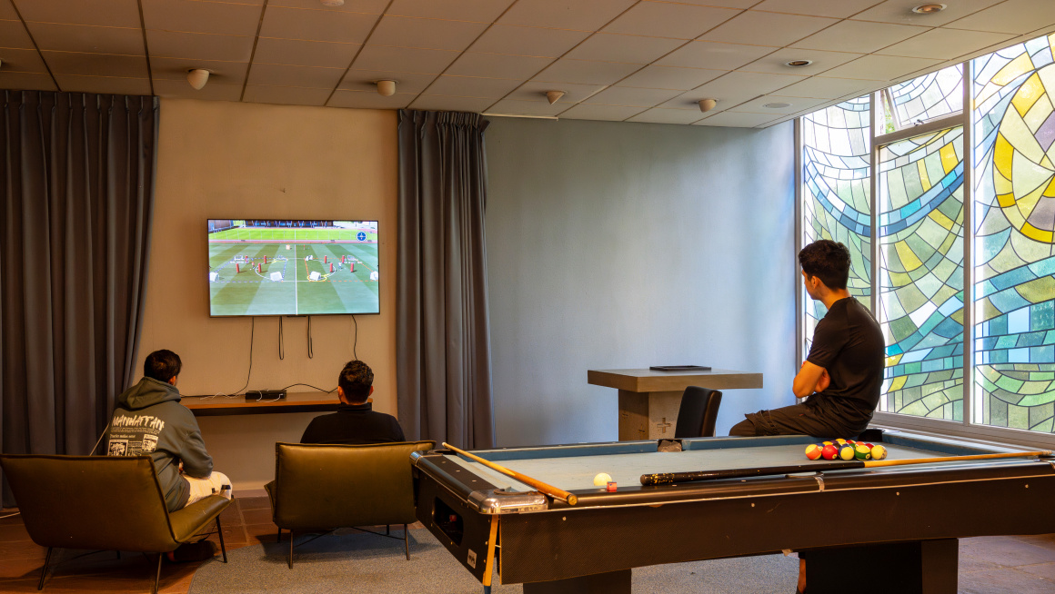 Jonge asielzoekers kijken tv in de recreatieruimte van het azc