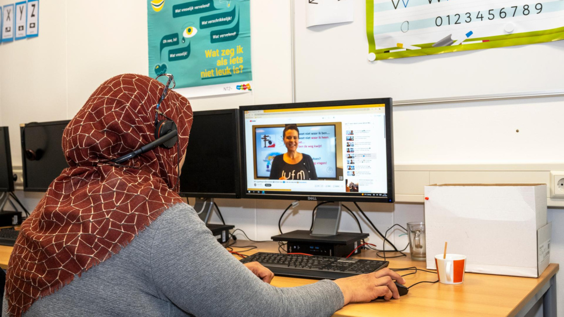 Vrouw met koptelefoon over haar hoofddoek zit achter de computer te werken