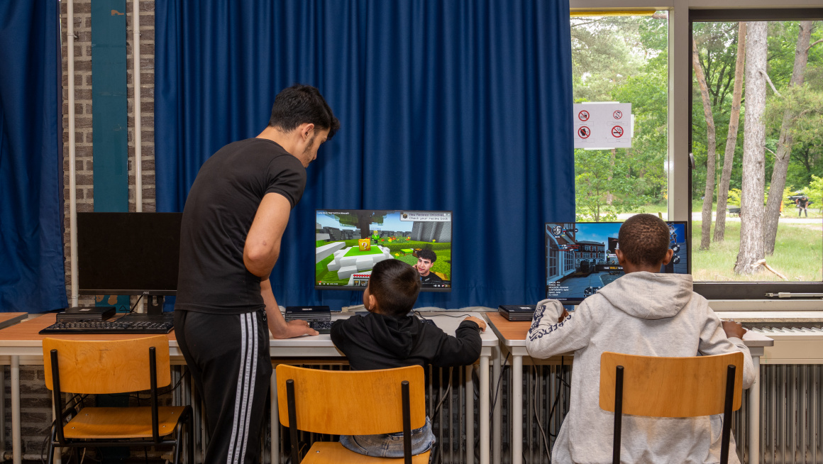 twee kinderen spelen een game op de computer terwijl een volwassene toekijkt