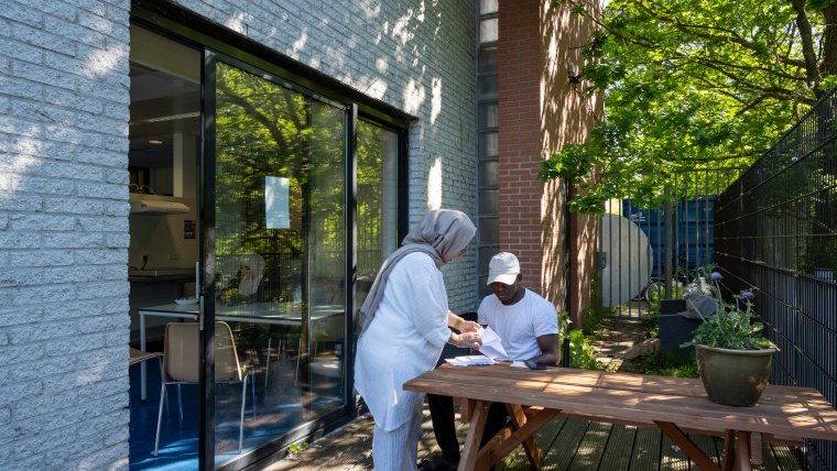 Medewerkster en asielzoeker hebben een gesprek aan de picknicktafel in de tuin van de noodopvang