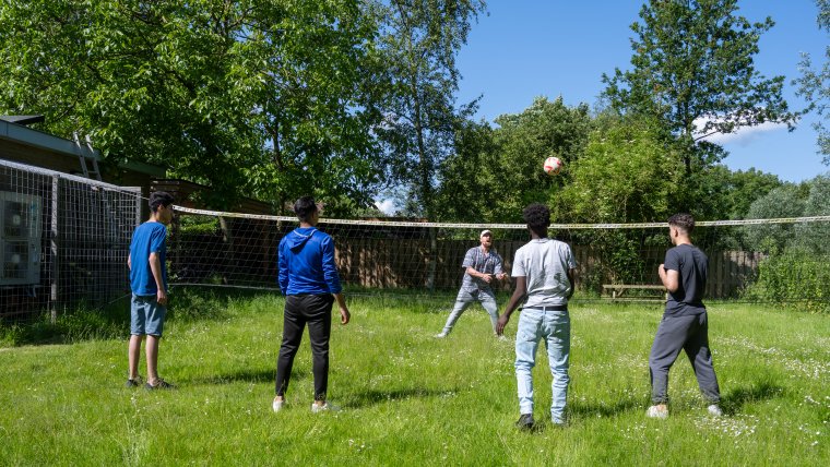 4 minderjarige jongens spelen volleybal in de tuin met een medewerker