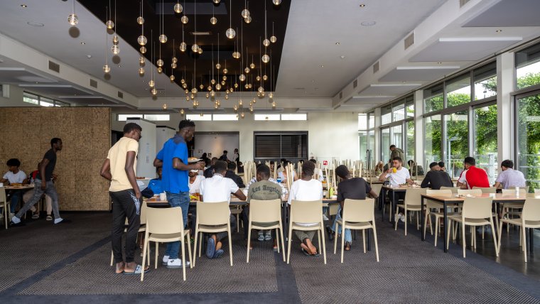 De eetzaal zit vol met minderjarige jongens die aan het lunchen zijn.