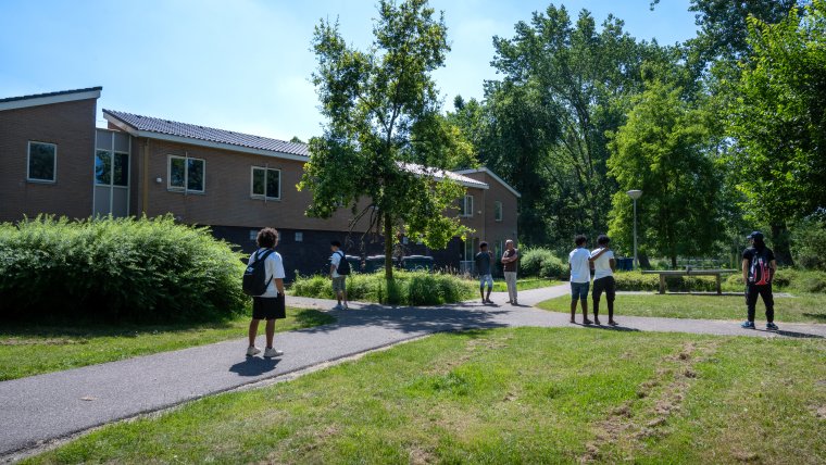 Diverse minderjarige jongens lopen over de paden in het groen rondom hun opvanglocatie.