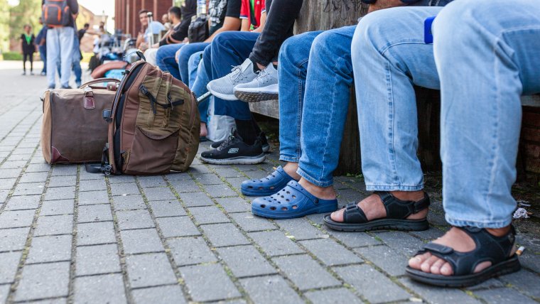 Op een lange rij zie je de benen en bagage van wachtenden in Ter Apel