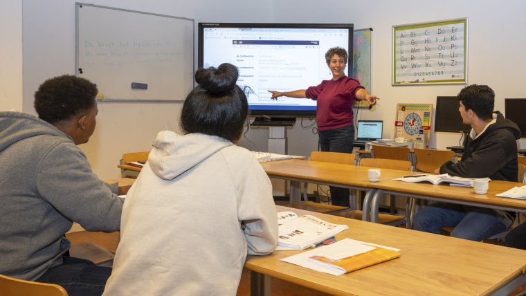 Vrijwilliger geeft Nederlandse les aan 3 asielzoekers in leslokaal