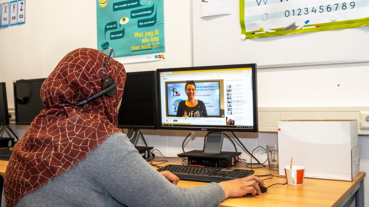Vrouw met koptelefoon over haar hoofddoek zit achter de computer te werken