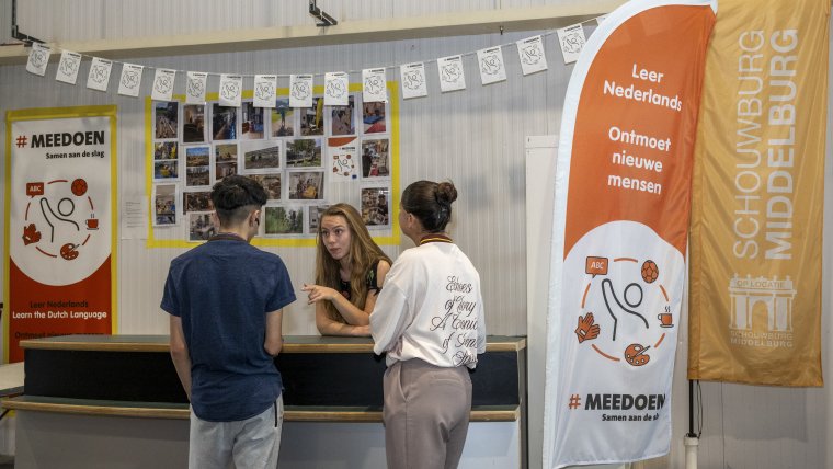 een medewerker staat aan de meedoenbalie twee bewoners te woord
