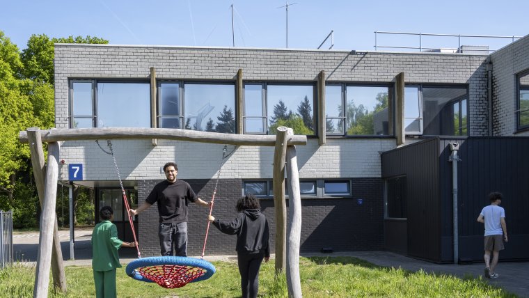 Twee kinderen en een bewoner op een speeltoestel in de tuin van coa locatie Rijsbergen