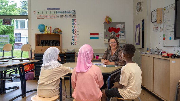 3 kinderen op school met de juf in het klaslokaal