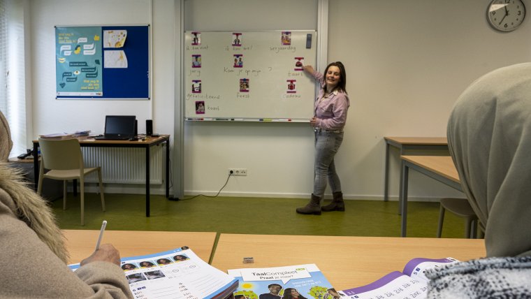 medewerkster geeft bewoners les in nederlandse taal in een klaslokkal, ze wijst iets aan op het bord