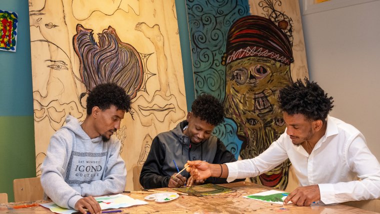drie mannelijke statushouders zitten aan tafel samen te schilderen en tekenen
