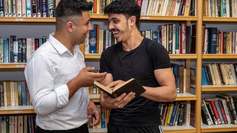 bewoner en begeleider met boek in de bibliotheek, ze hebben lol samen