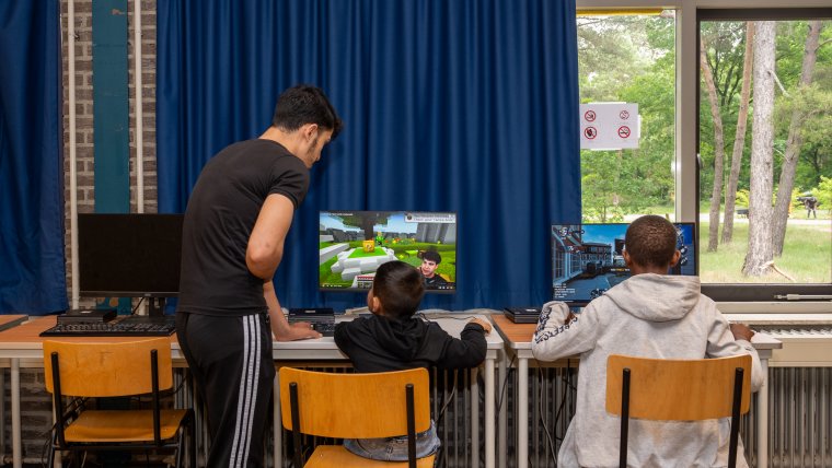 twee kinderen spelen een game op de computer terwijl een volwassene toekijkt