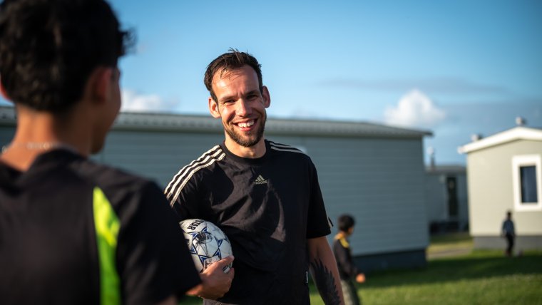 Sportcoach met voetbal onder arm lacht naar bewoner