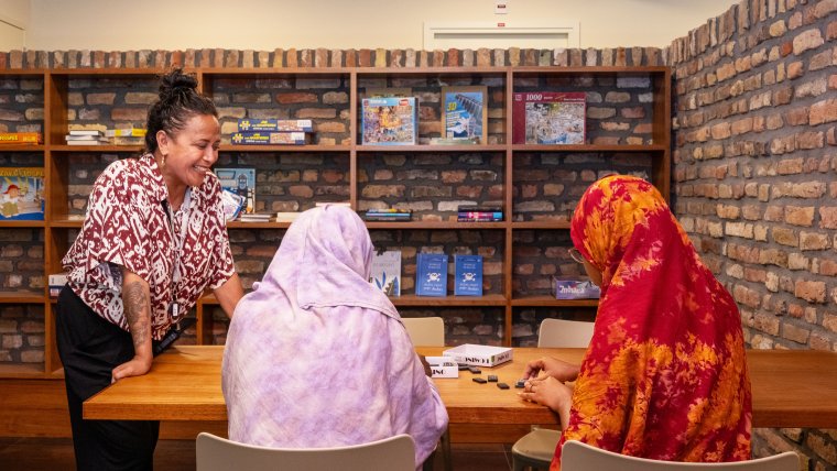 Vrouwelijke medewerker en bewoners doen een spelletje domino aan tafel