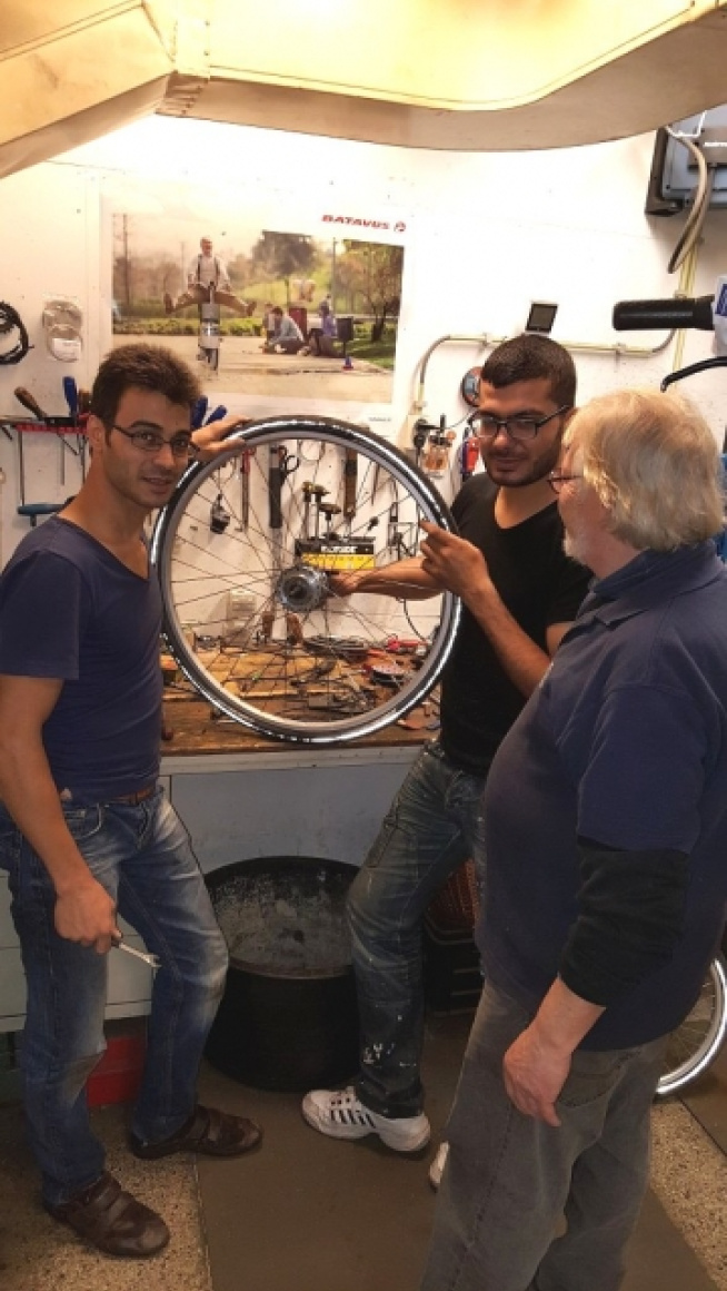 twee jongeren werken aan een fiets en een oudere meneer staat erbij
