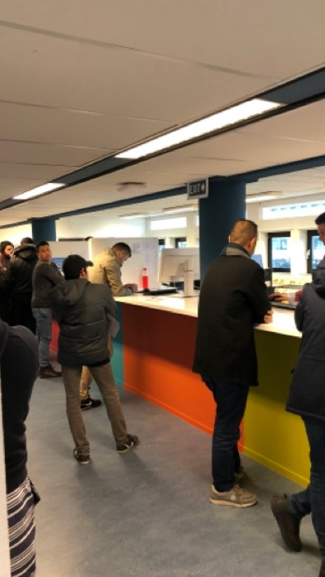 informatiebalie met daarvoor bewoners en onder de informatiebalie vrolijke kleuren, geel, oranje en blauw