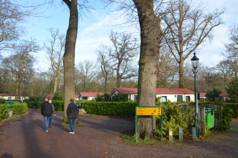 witte woonunits met rode daken en her en der grote bomen en heggen, op de voorgrond lopen 3 mannen