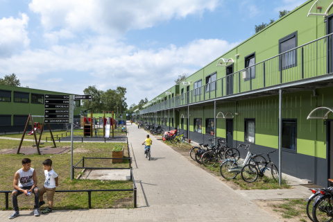 Groene gebouwen met twee verdiepingen, fietsen, gras en speeltuin met kinderen ervoor