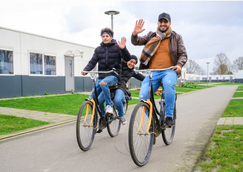 Twee zwaaiende mannen op de fiets op het terrein van he azc.