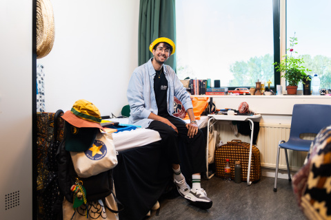 Jongeman met gele hoed zit op zijn bed in azc Leiden
