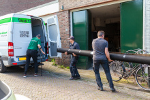 Bewoner draagt samen met andere man een rol tapijt een verhuisbusje in. 