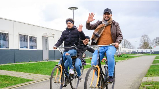 Twee zwaaiende mannen op de fiets op het terrein van he azc.