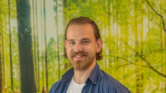 Man met baard staat voor muur met behang van een bos